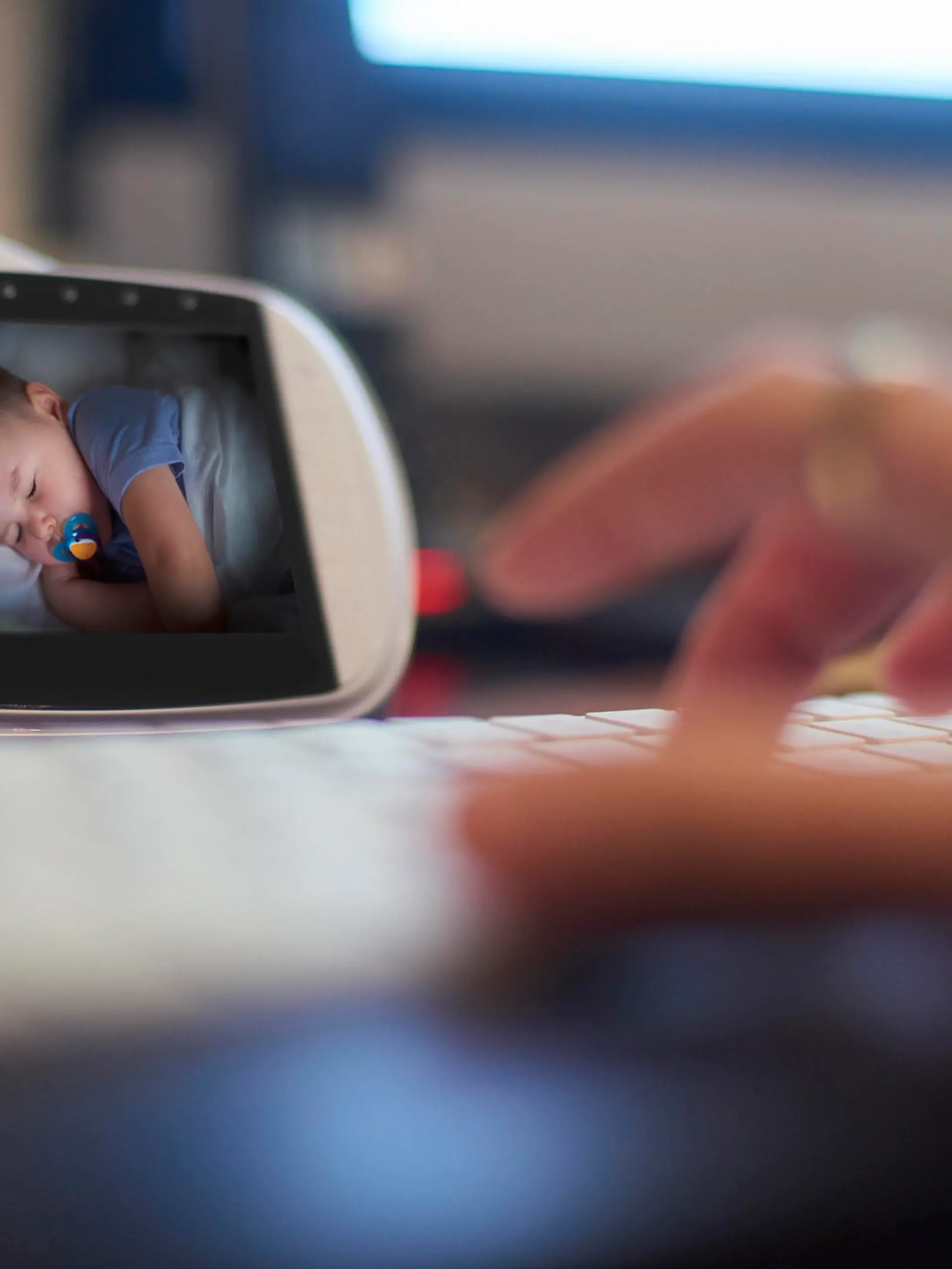 Baby monitor on the desk in home office. Parent is getting on with some work as the baby sleeps.
