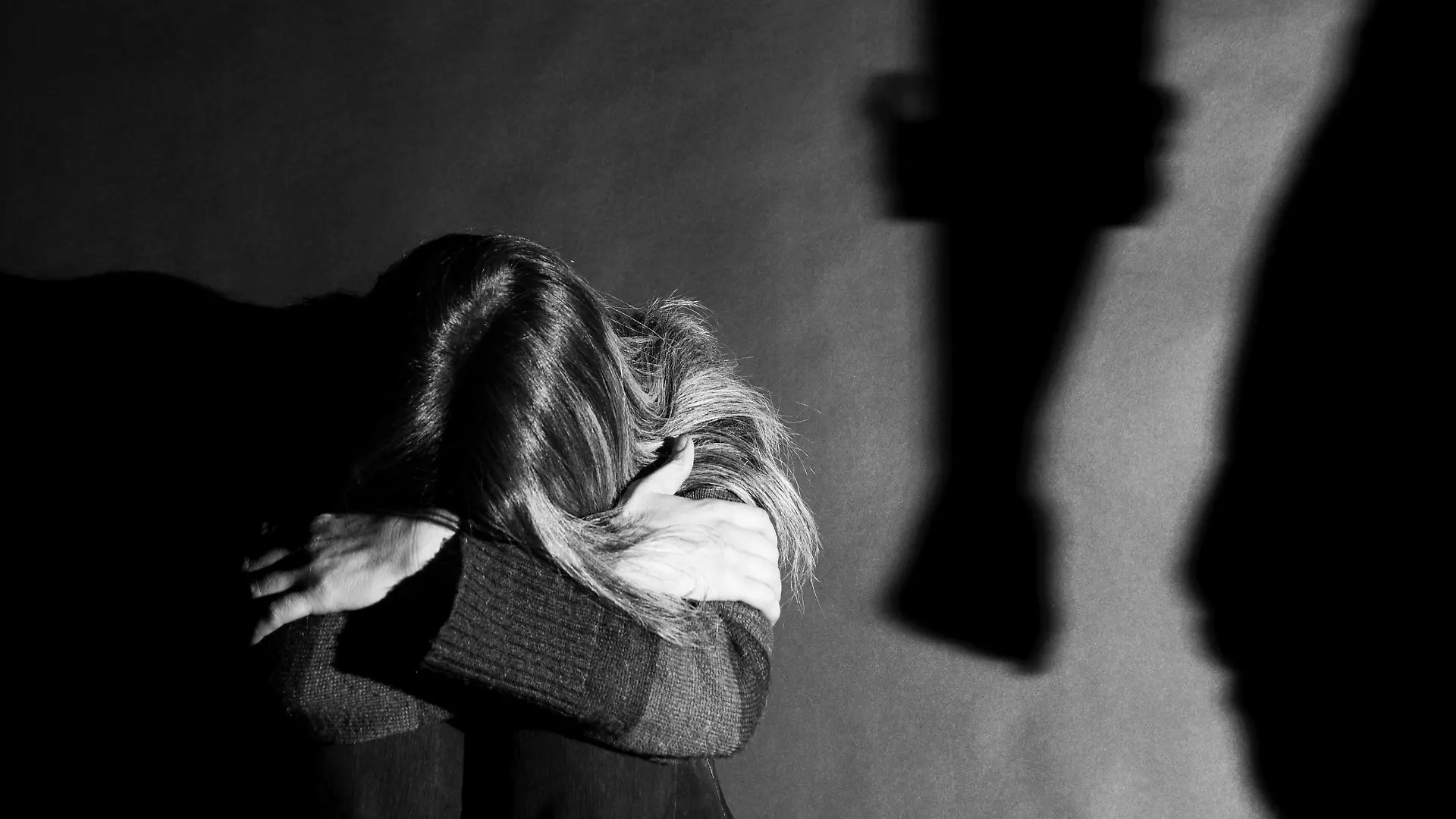 Eine Frau kauert auf dem Boden und scheint sich vor einer anderen Person schützen zu wollen.