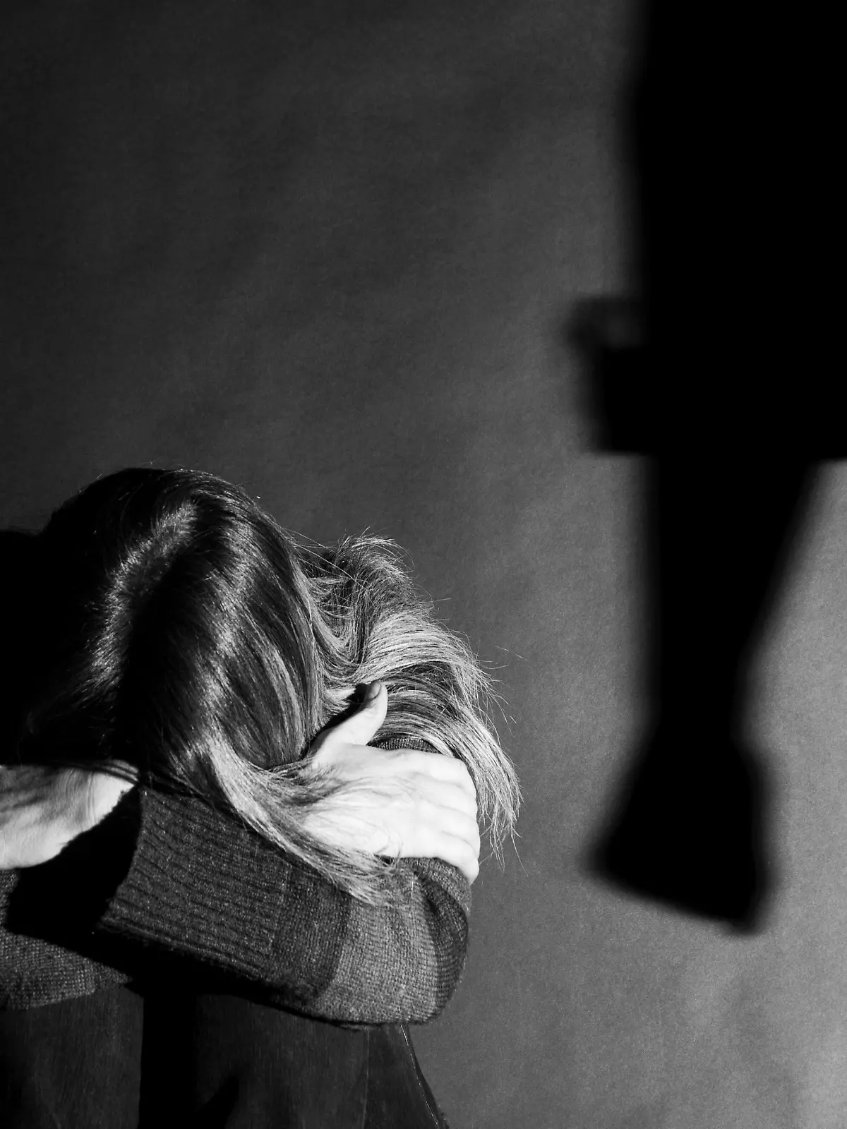 Eine Frau kauert auf dem Boden und scheint sich vor einer anderen Person schützen zu wollen.