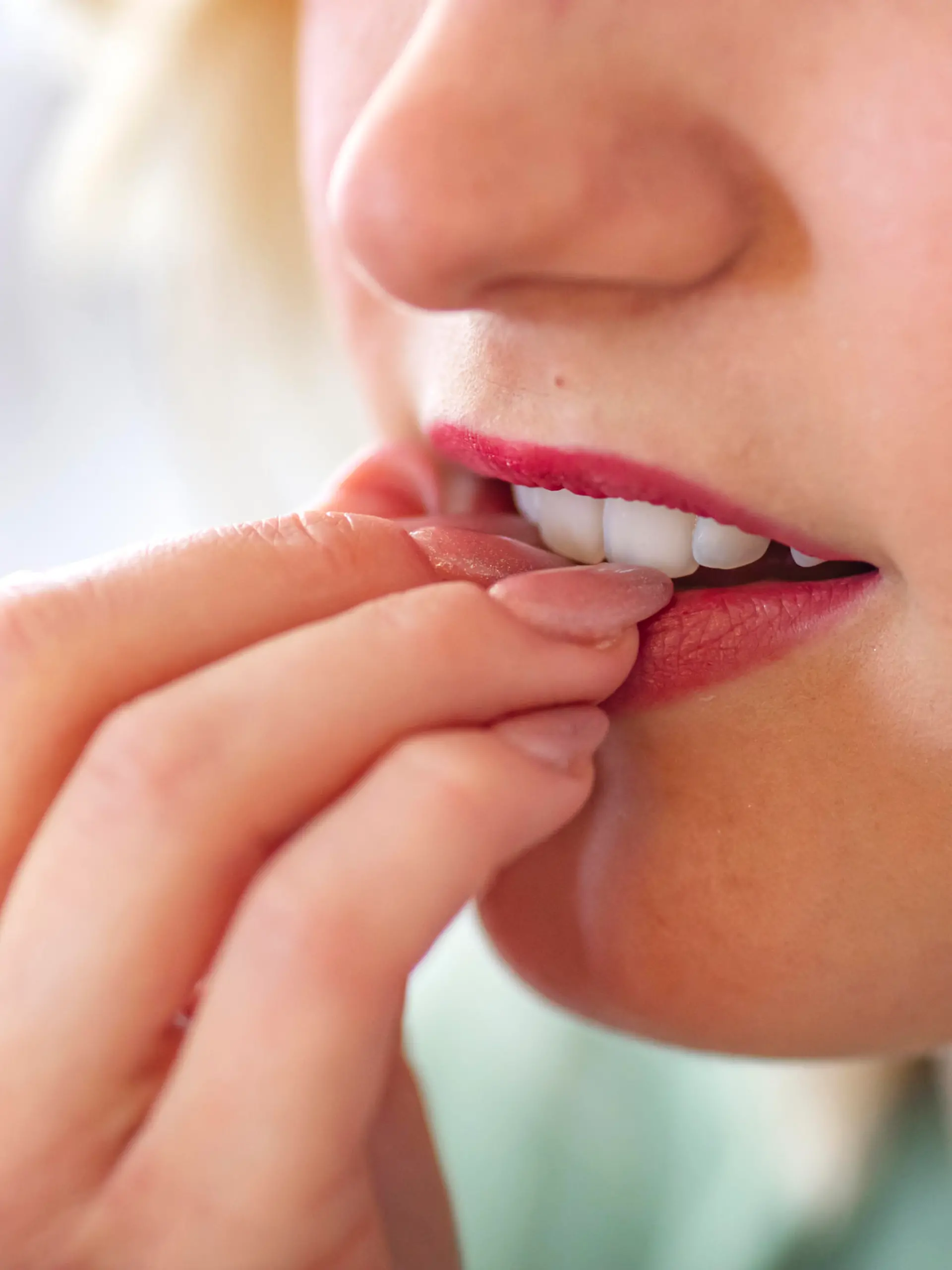 Close-up view on the woman biting nails. Close up of a female mouth biting her fingers. Woman bites his nails from the experience. Nervous young woman biting her nails on gray background