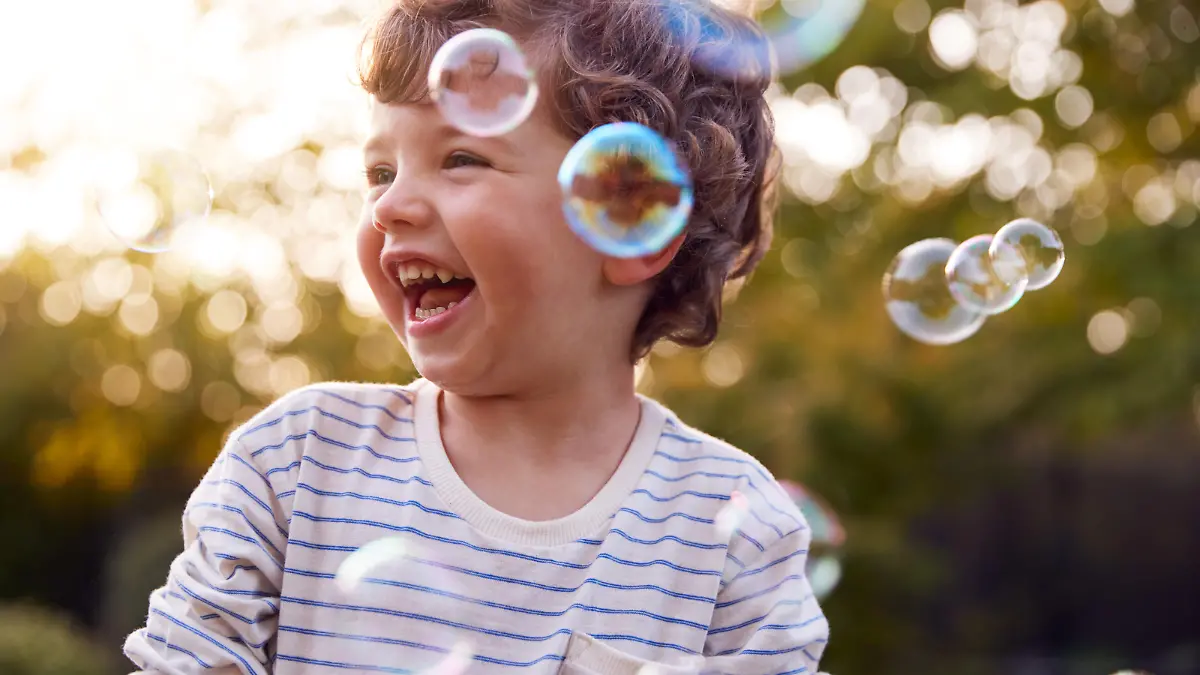 Young Boy Having Fun In Garden Chasing And Bursting Bubbles