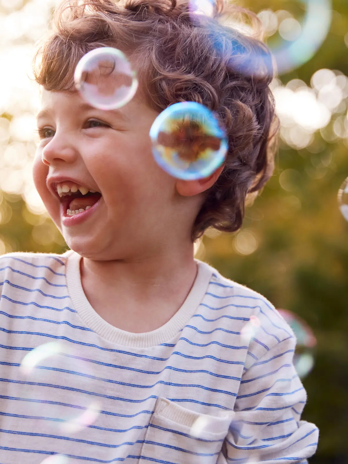 Young Boy Having Fun In Garden Chasing And Bursting Bubbles
