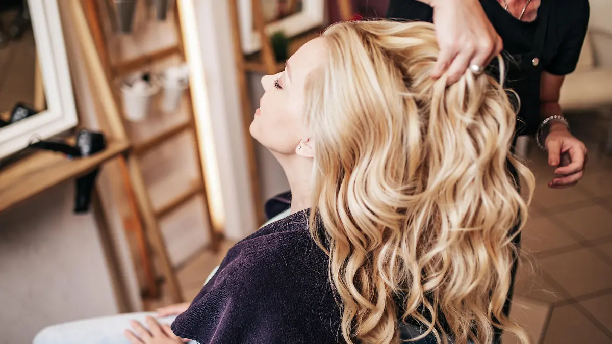 Professional hairdresser making a beautiful hairstyle of young adult woman after dyeing hair and making highlights in hair salon. Modern lifestyle concept.