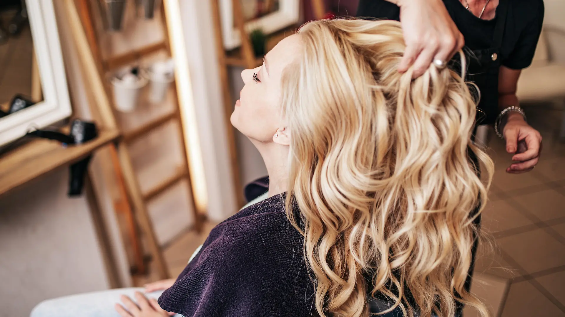 Professional hairdresser making a beautiful hairstyle of young adult woman after dyeing hair and making highlights in hair salon. Modern lifestyle concept.