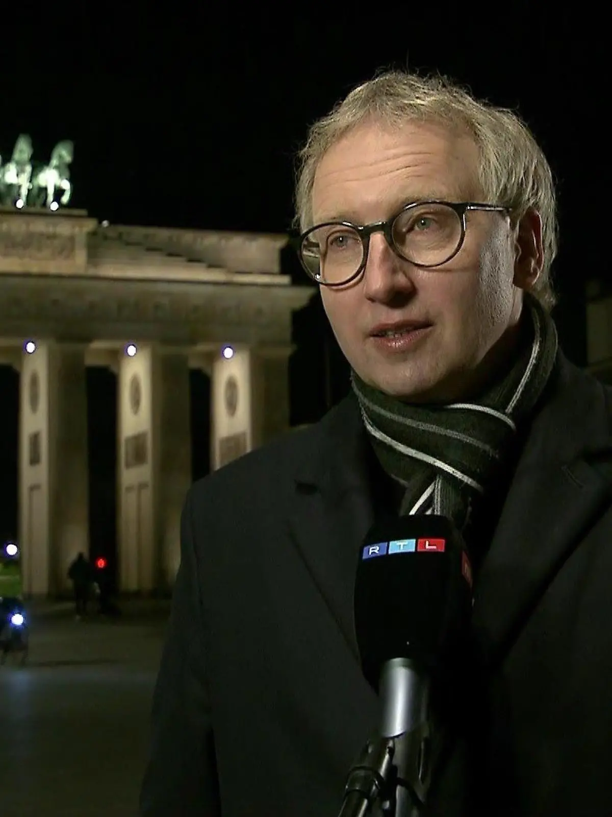 Johannes Varwick steht nach Sonnenuntergang vor dem beleuchteten Brandenburger Tor in Berlin.