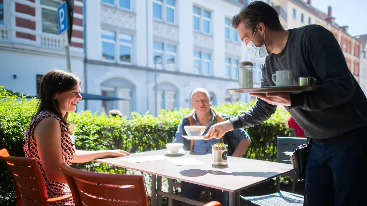 31.05.2021, Niedersachsen, Hannover: Kellner Alejandro serviert auf der Außenterrasse vom Café Mezzo an der Lister Meile Kaffee für die Gäste Mirella und Holger. In Niedersachsen wurde die Corona-Verordnung auch für die Gastronomie gelockert. Bei entsprechenden Inzidenzen darf die Innengastronomie wieder öffnen und die Testpflicht im Bereich der Außengastronomie entfällt. Foto: Julian Stratenschulte/dpa +++ dpa-Bildfunk +++