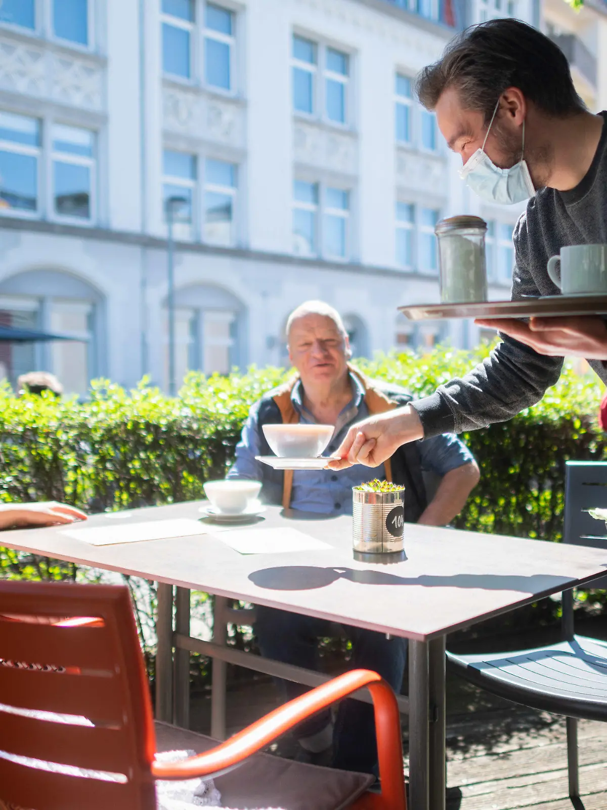 31.05.2021, Niedersachsen, Hannover: Kellner Alejandro serviert auf der Außenterrasse vom Café Mezzo an der Lister Meile Kaffee für die Gäste Mirella und Holger. In Niedersachsen wurde die Corona-Verordnung auch für die Gastronomie gelockert. Bei entsprechenden Inzidenzen darf die Innengastronomie wieder öffnen und die Testpflicht im Bereich der Außengastronomie entfällt. Foto: Julian Stratenschulte/dpa +++ dpa-Bildfunk +++