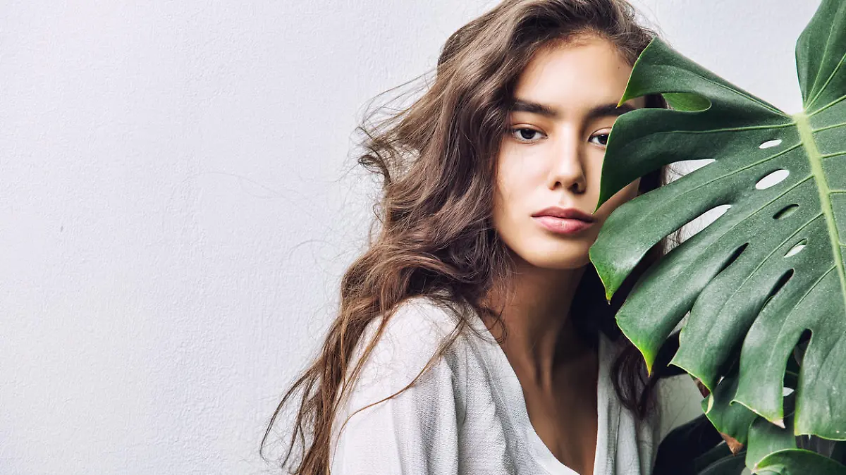 Young beautiful girl model Asian brunette with long hair posing in Studio with tropical plant on isolated background