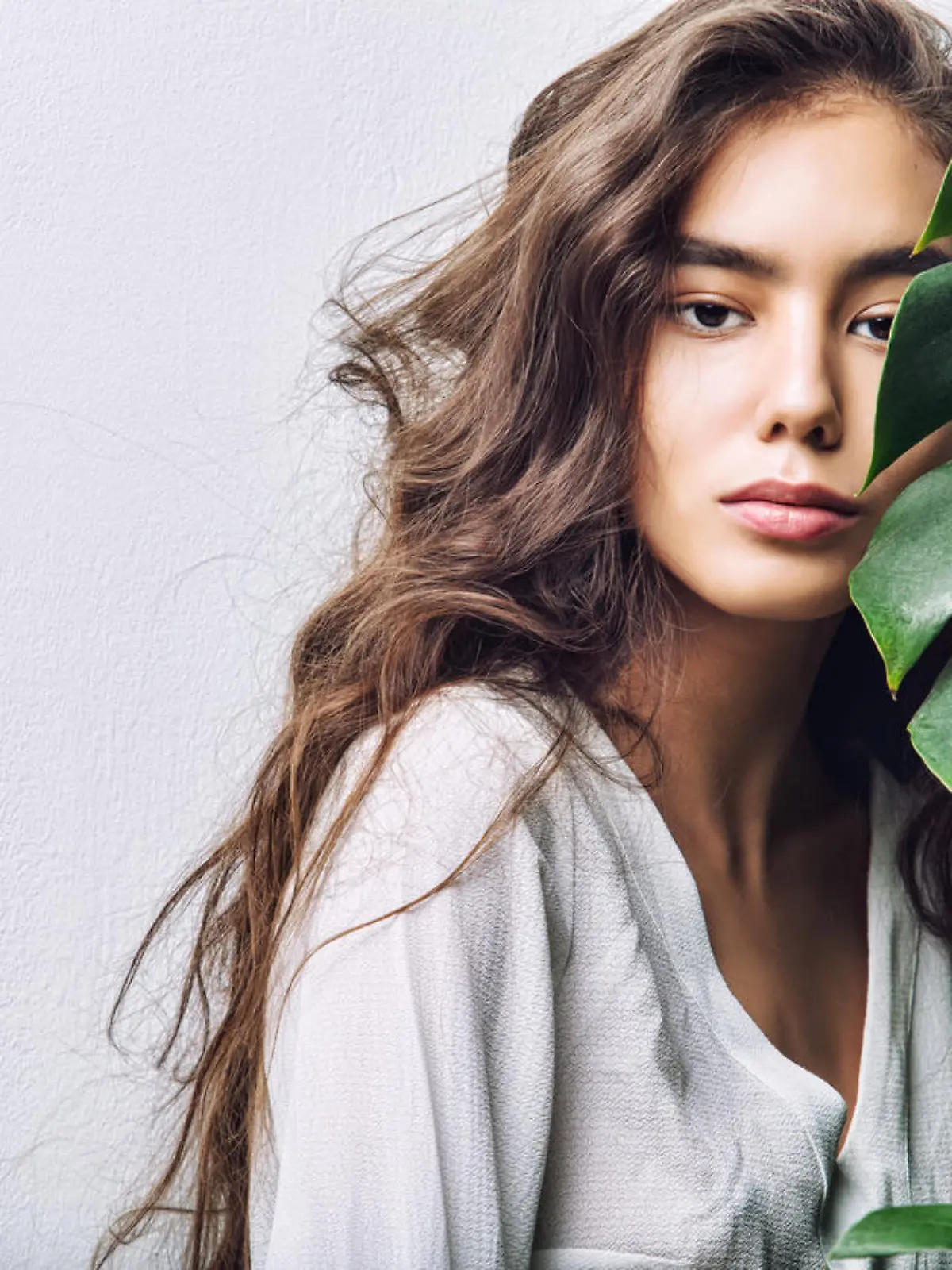 Young beautiful girl model Asian brunette with long hair posing in Studio with tropical plant on isolated background