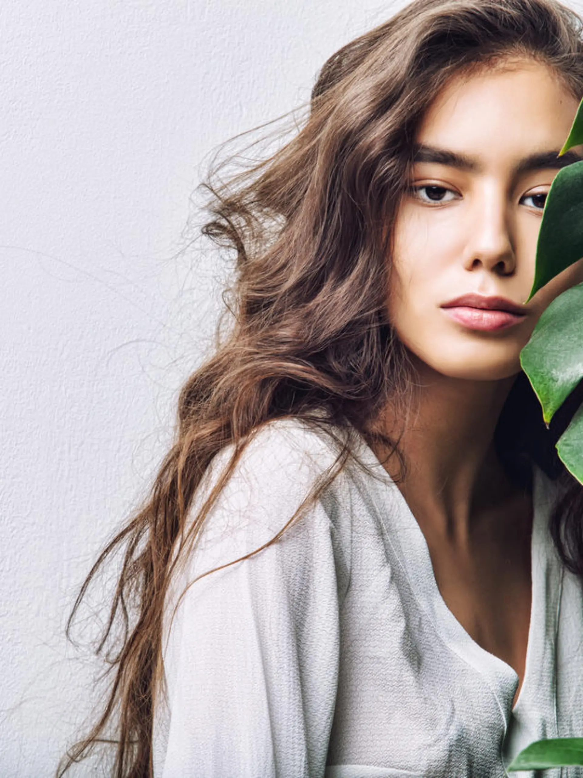 Young beautiful girl model Asian brunette with long hair posing in Studio with tropical plant on isolated background