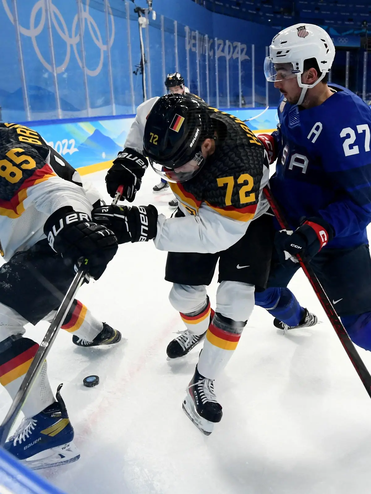 2022 Beijing Olympics - Ice Hockey - Men's Prelim. Round - Group A - United States v Germany - Wukesong Sports Centre, Beijing, China - February 13, 2022. Noah Cates of the United States in action with Marcel Brandt of Germany and Dominik Kahun of Germany. REUTERS/Annegret Hilse