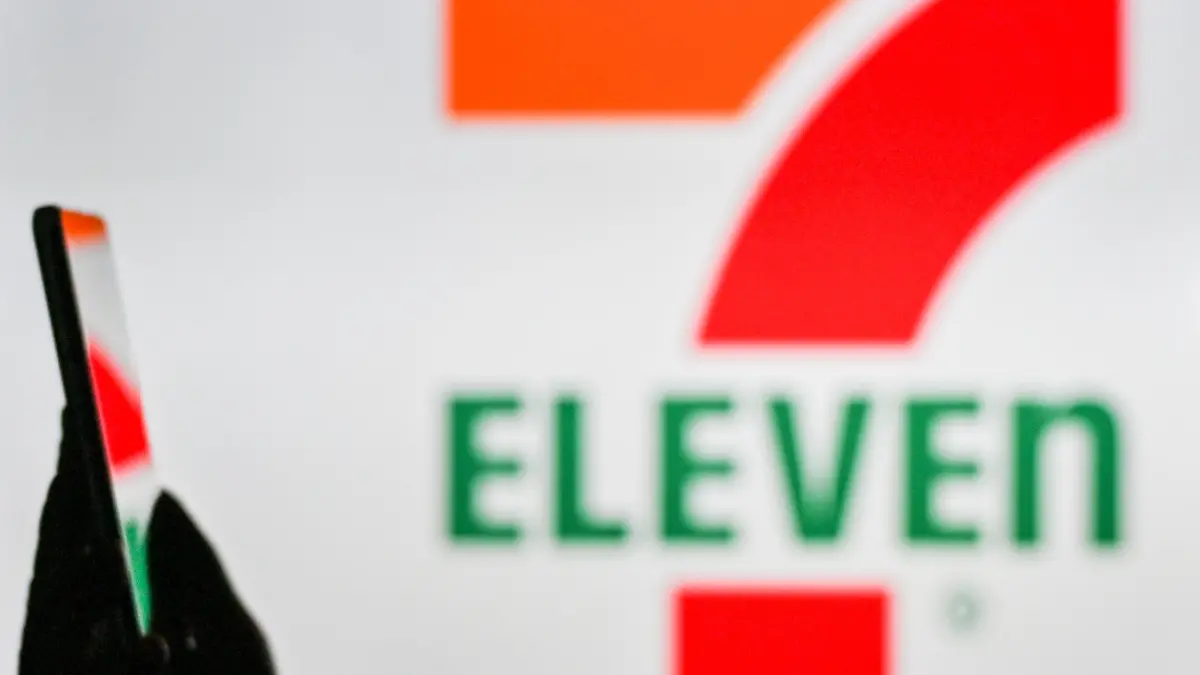 An image of a woman holding a cell phone in front of the 7-Eleven logo displayed on a computer screen. On Tuesday, January 12, 2021, in Edmonton, Alberta, Canada. (Photo by Artur Widak/NurPhoto)