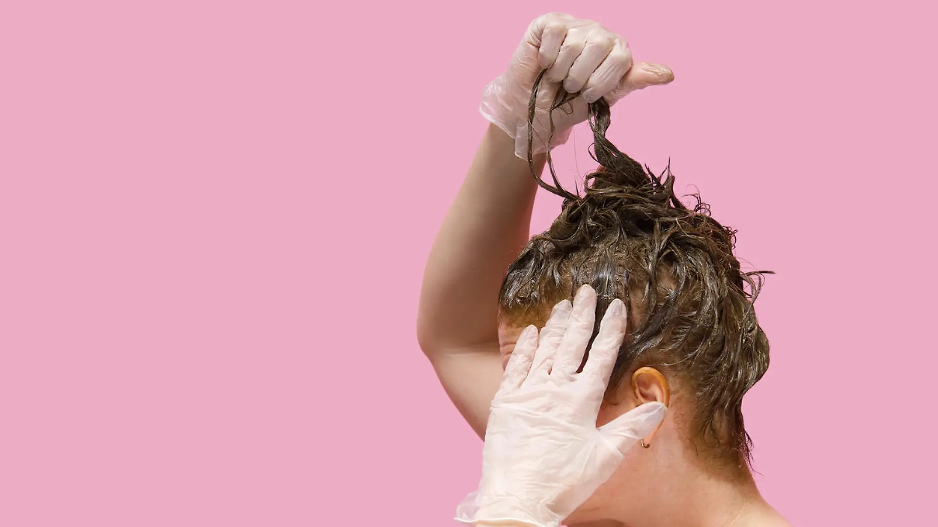 Home beauty industry in coronavirus pandemic time. young woman in gloves stays at home and painting her hairs on pink background
