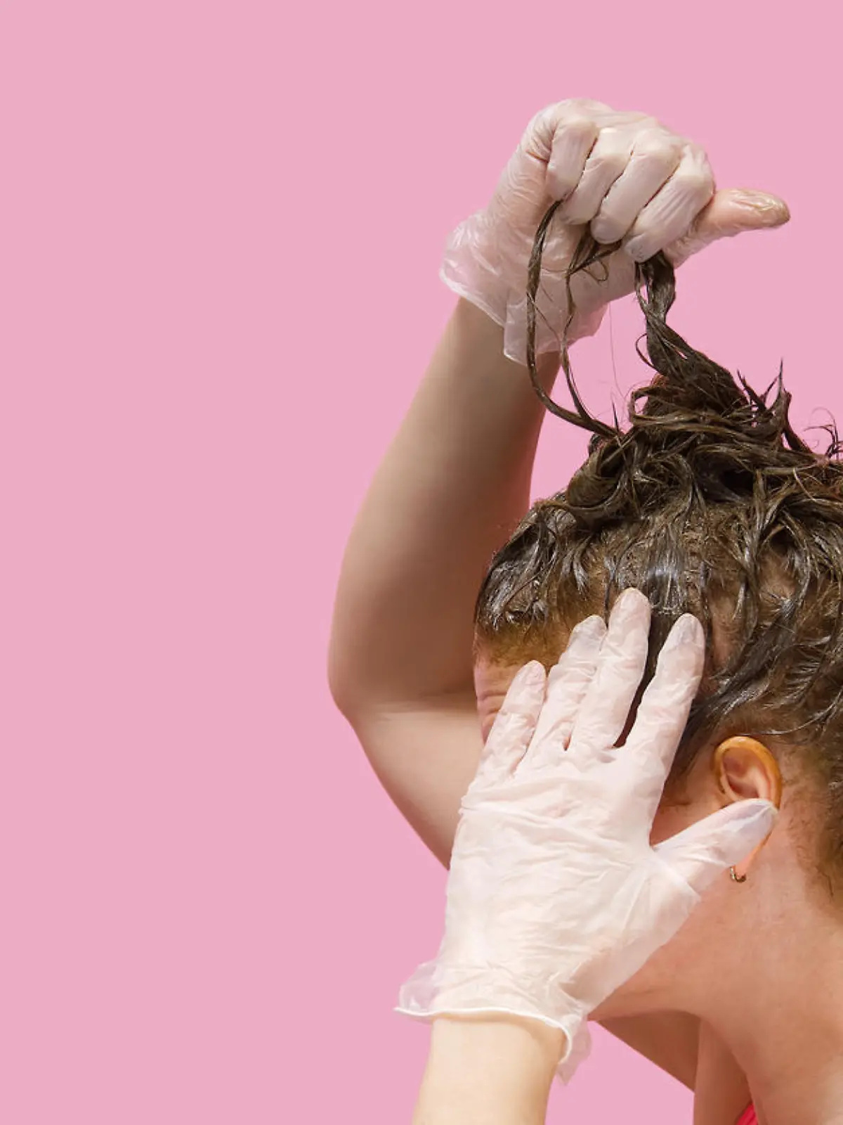 Home beauty industry in coronavirus pandemic time. young woman in gloves stays at home and painting her hairs on pink background