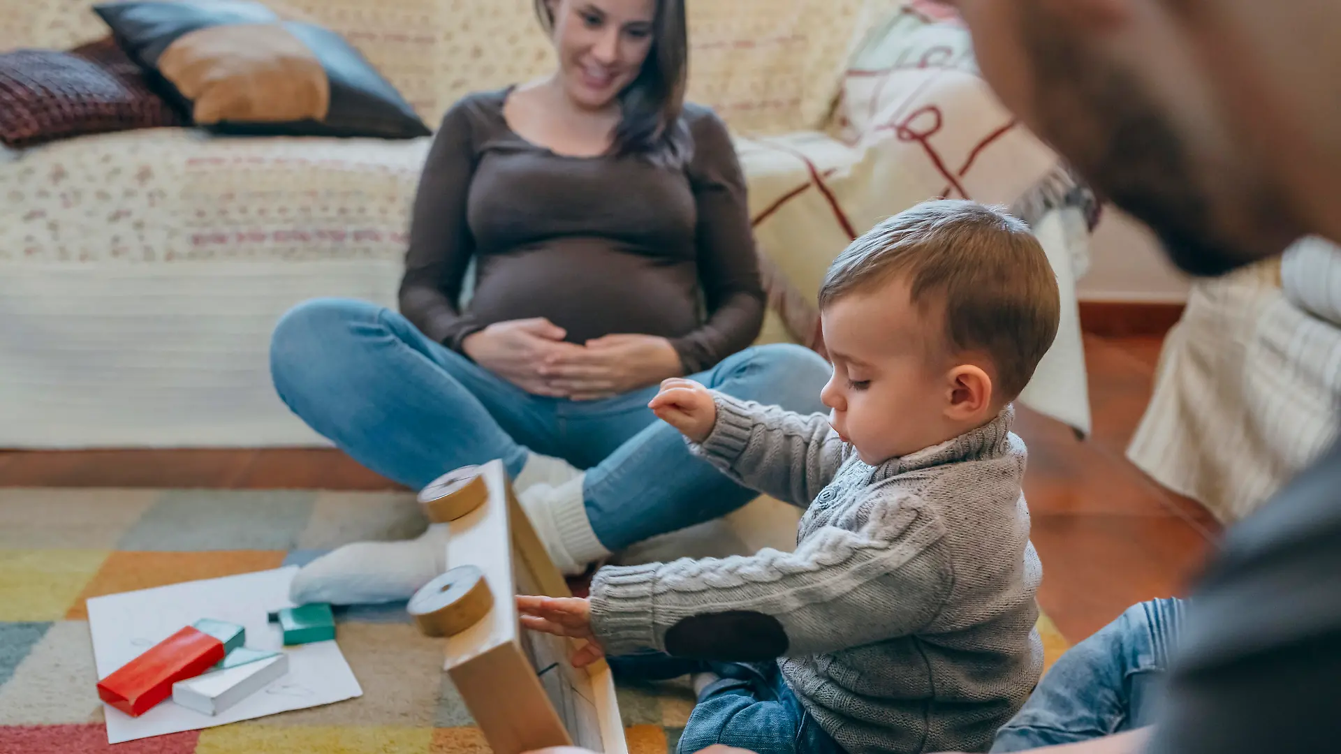 Young father playing with his toddler a wooden game building in the living room while the mother is looking at them
