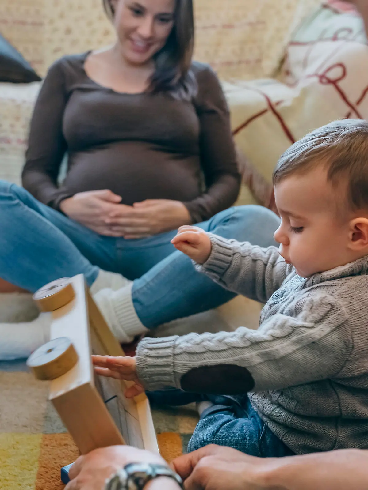 Young father playing with his toddler a wooden game building in the living room while the mother is looking at them