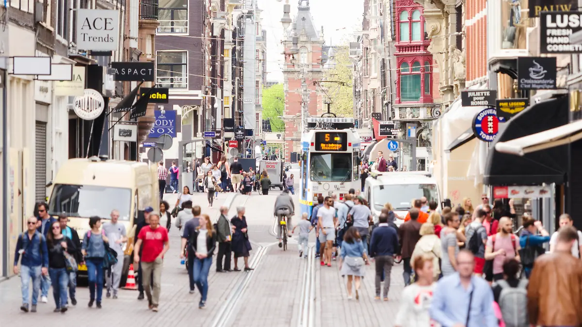 The famous Leidsestraat with the Leidseplein and city theatre in the background. Tourists and locals are walking, a tram is approaching.
