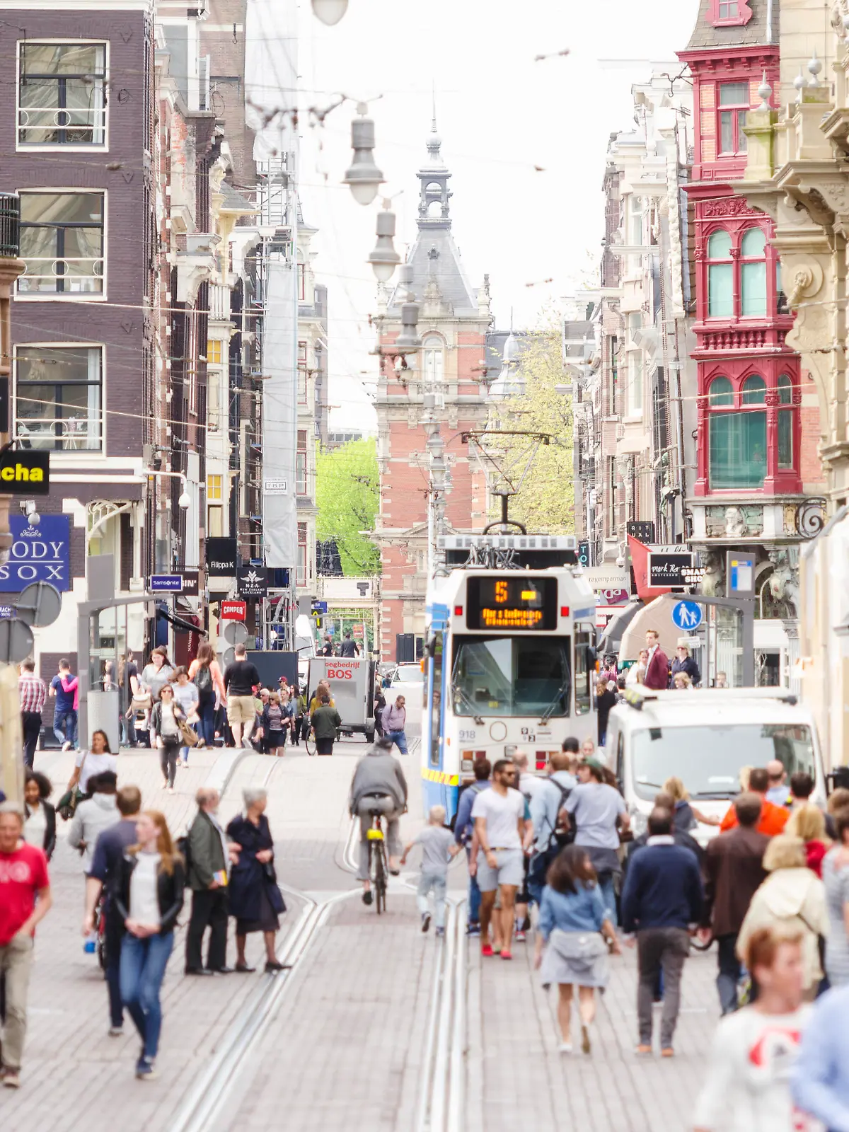 The famous Leidsestraat with the Leidseplein and city theatre in the background. Tourists and locals are walking, a tram is approaching.