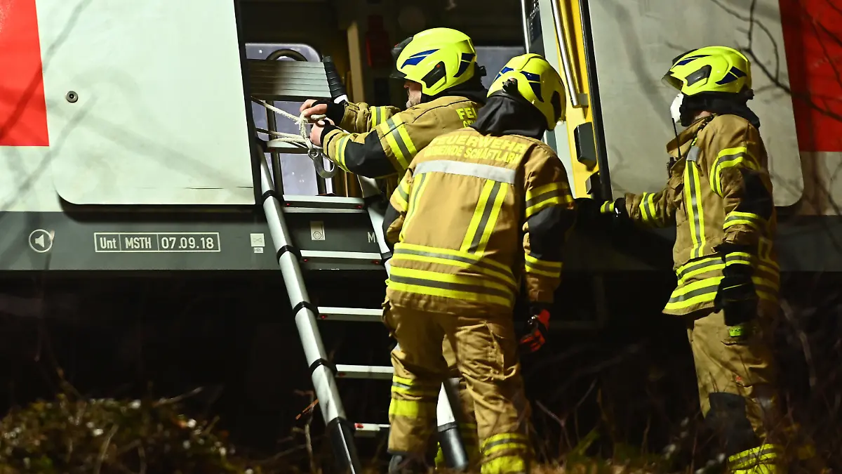 14.02.2022, Bayern, Schäftlarn: Feuerwehrleute befestigen eine Leiter an einem verunfallten S-Bahnwagen. Beim Zusammenstoß zweier S-Bahnen im Landkreis München sind am Montag ein Mensch getötet und mehr als zehn verletzt worden. Es habe eine niedrige zweistellige Zahl an Verletzten gegeben, berichtete ein Sprecher des Münchner Polizeipräsidiums. Foto: Lennart Preiss/dpa +++ dpa-Bildfunk +++
