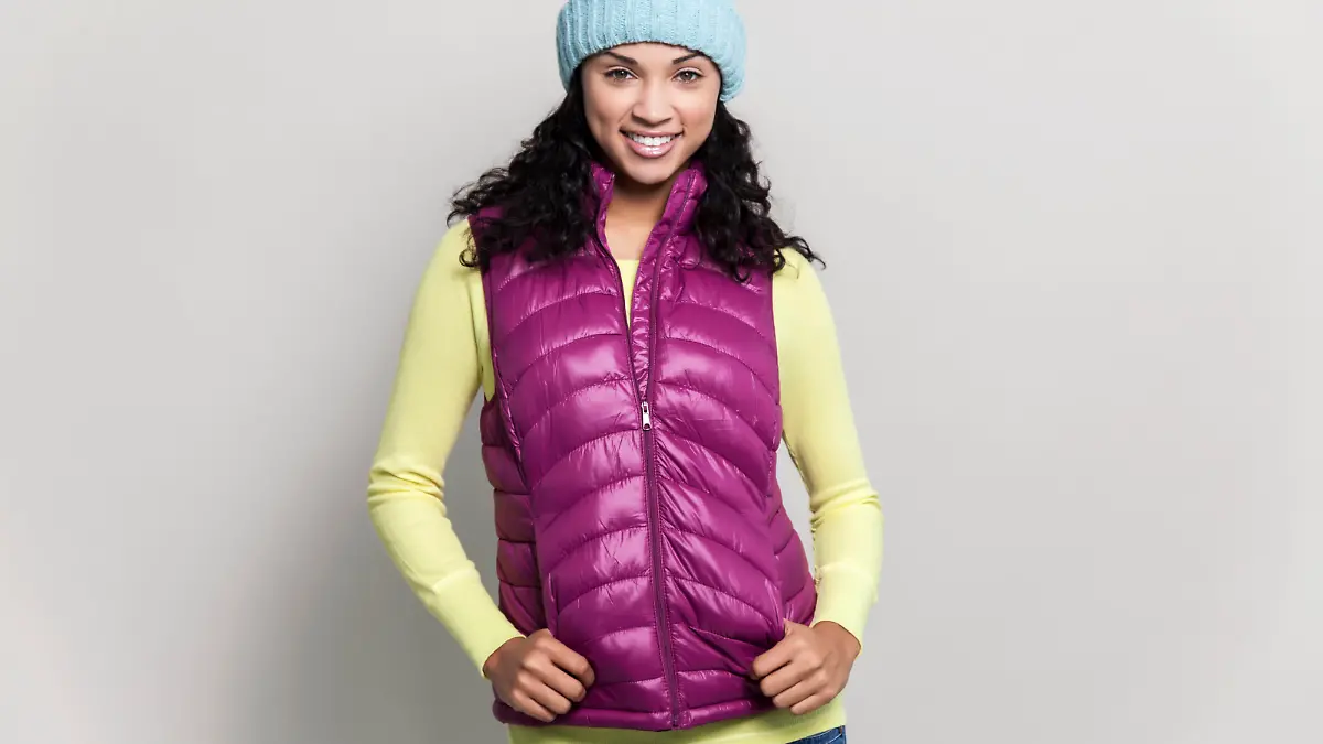 Beautiful mixed race woman with black curly hair wearing a blue winter hat, purple scarf, purple vest and yellow sweater. The model has pretty green eyes, and a beautiful smile.