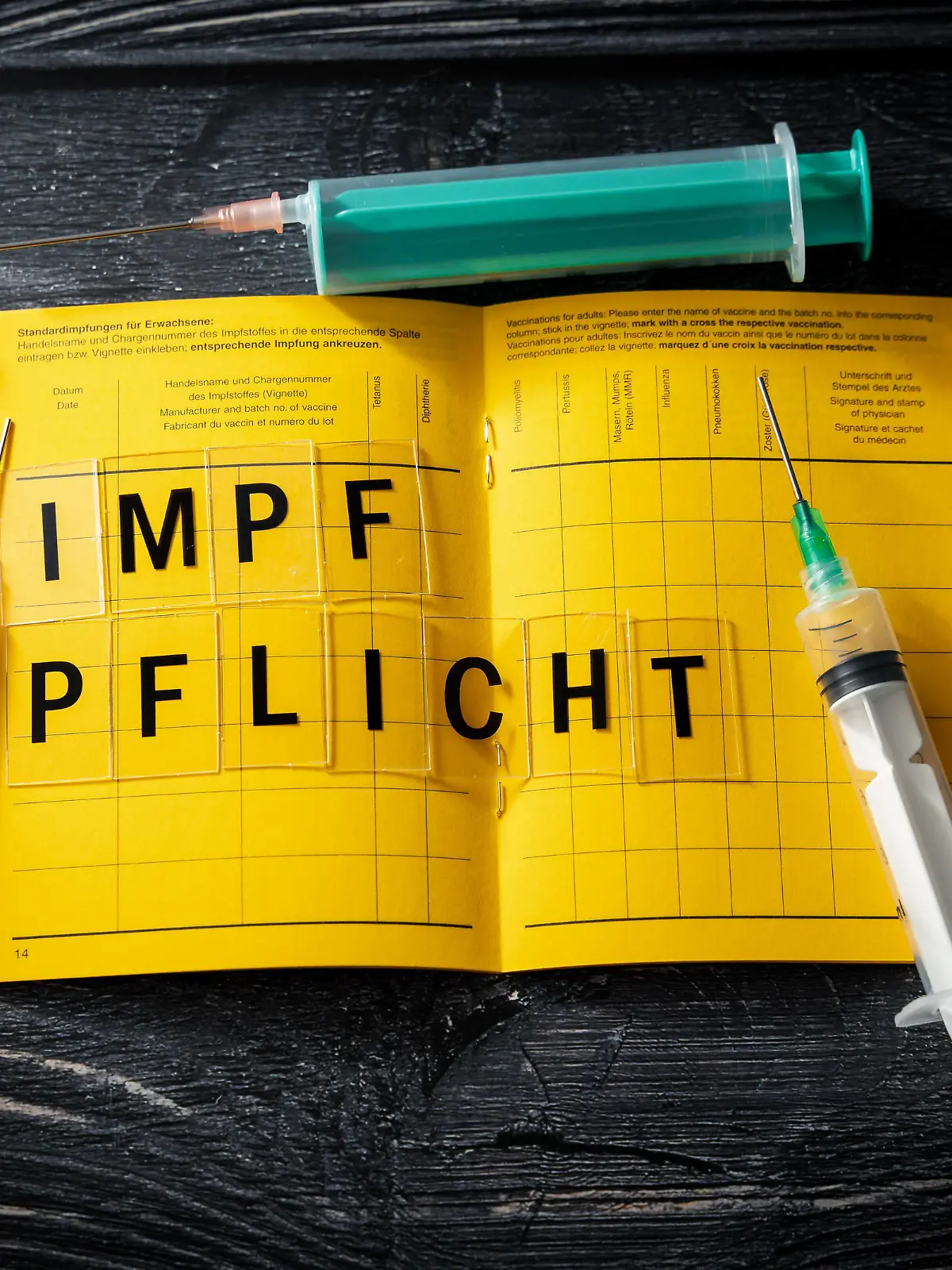  Germany - 26 January 2022: Yellow vaccination card with the inscription vaccination obligation together with three syringes - symbol image General Covid 19 coronavirus obligation to vaccinate *** Gelber Impfpass mit der Aufschrift Impfpflicht zusammen mit drei Spritzen - Symbolbild Allgemeine Covid 19 Coronavirus Pflicht zur Impfung
