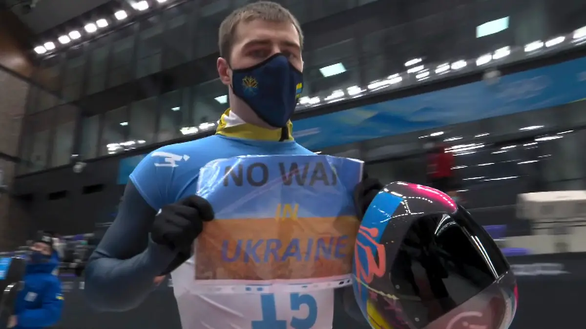 HANDOUT - 11.02.2022, China, Peking: In diesem Videobild hält der Ukrainer Wladislaw Heraskewitsch ein Schild mit der Aufschrift «Kein Krieg in der Ukraine», nachdem er einen Lauf beim Skeleton-Wettbewerb der Männer bei den Olympischen Winterspielen 2022 beendet hat (NBC via AP) (zu «Skeletonpilot protestiert bei Olympia: «Kein Krieg in der Ukraine»») Foto: Uncredited/NBC/AP/dpa - ACHTUNG: Nur zur redaktionellen Verwendung im Zusammenhang mit der aktuellen Berichterstattung innerhalb der nächsten 14 Tage und nur mit vollständiger Nennung des vorstehenden Credits +++ dpa-Bildfunk +++