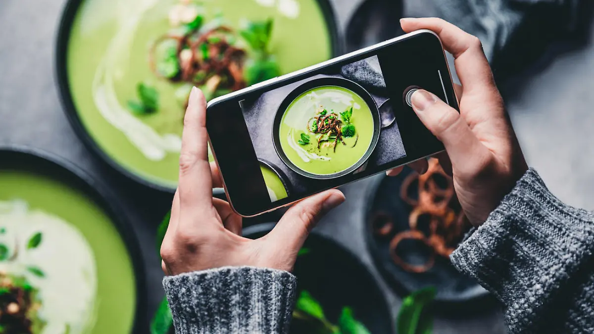 Close-up of a woman taking a photo of green cream soup with her mobile phone. Female hand photographing green soup.
