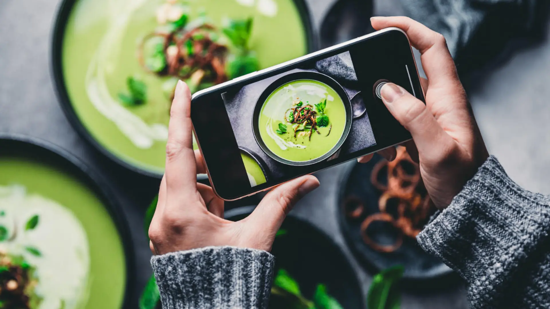 Close-up of a woman taking a photo of green cream soup with her mobile phone. Female hand photographing green soup.