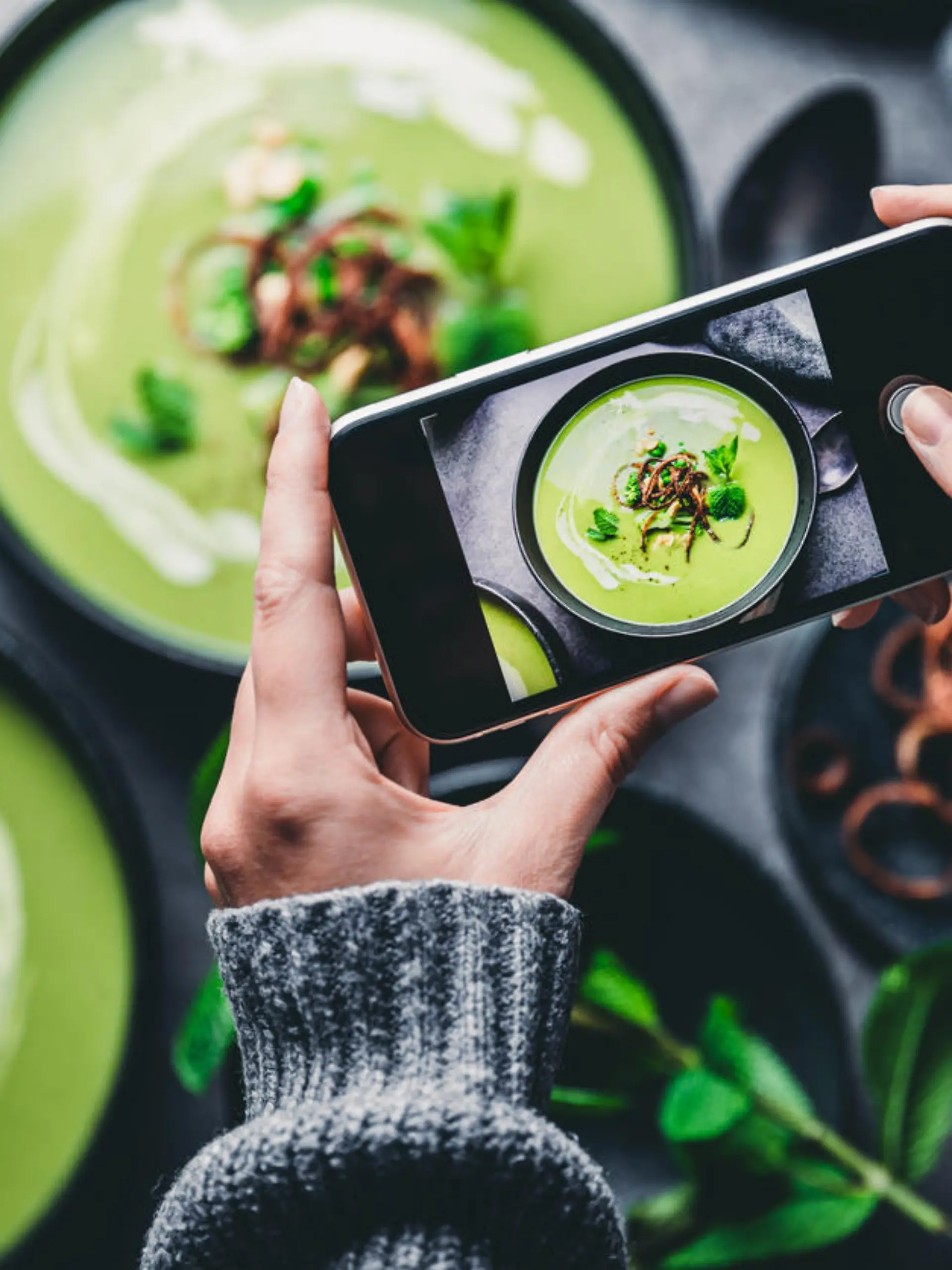 Close-up of a woman taking a photo of green cream soup with her mobile phone. Female hand photographing green soup.