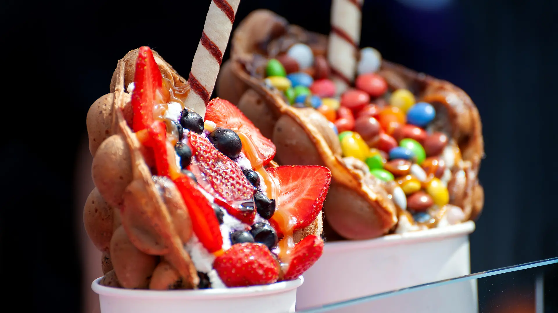 Cup with delicious sweet bubble waffle on dark background