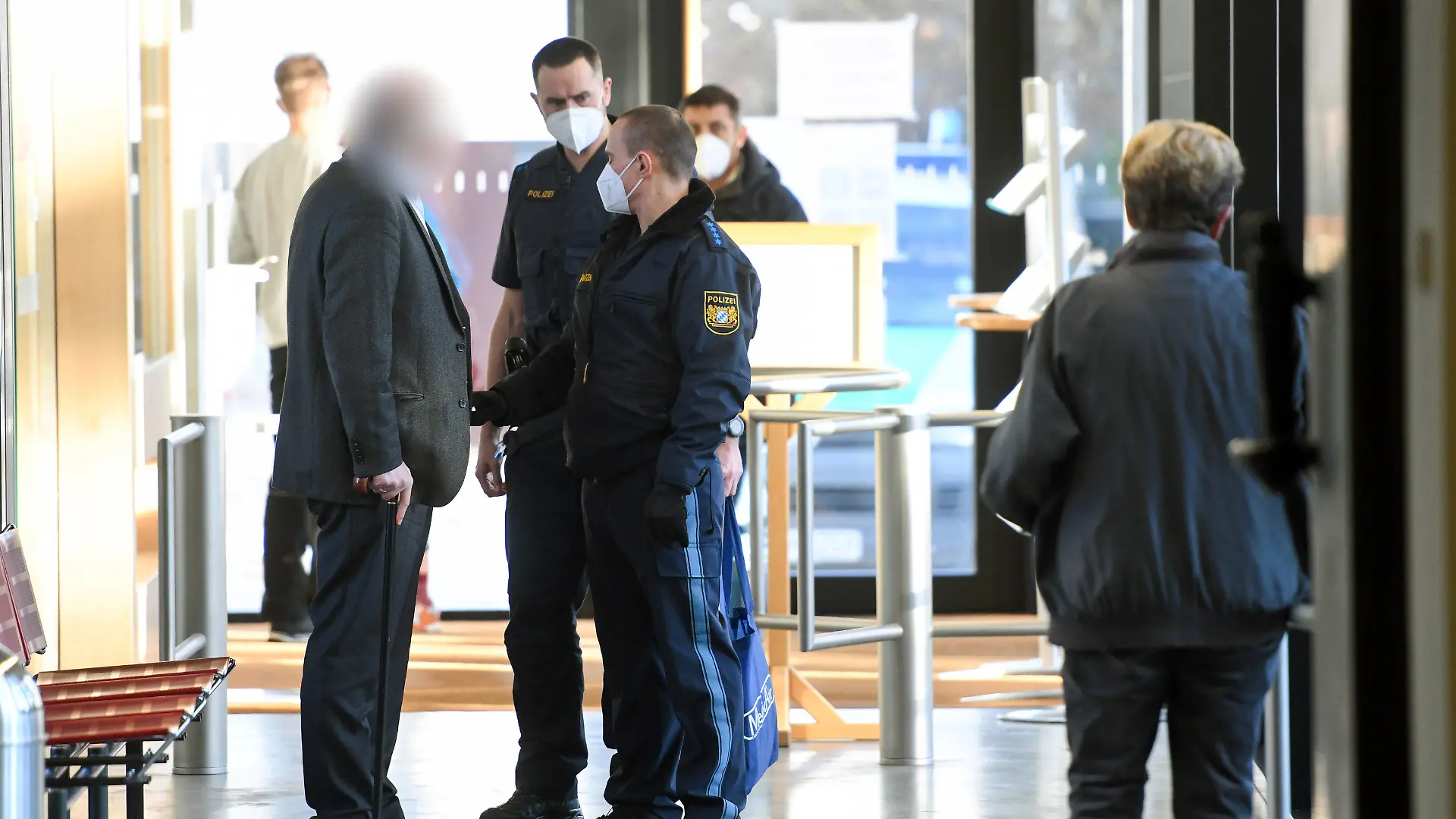 10.02.2022, Bayern, Traunstein: Der Angeklagte (vorne, l) wird kurz vor Prozessauftakt von Polizisten in das Landgericht Traunstein gebracht. Der Mann soll sich als Arzt ausgegeben und hunderte Patienten gegen Corona geimpft haben. Foto: Tobias Hase/dpa - ACHTUNG: Der Angeklagte wurde auf Wunsch seiner Anwältin gepixelt +++ dpa-Bildfunk +++