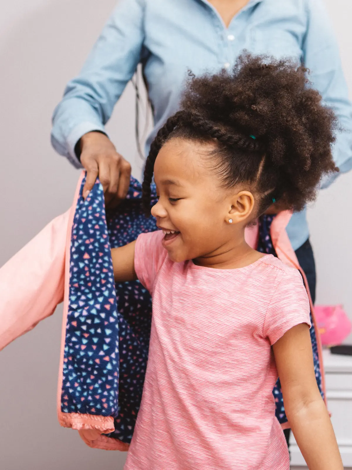 Little girl putting on her jacket to head out.