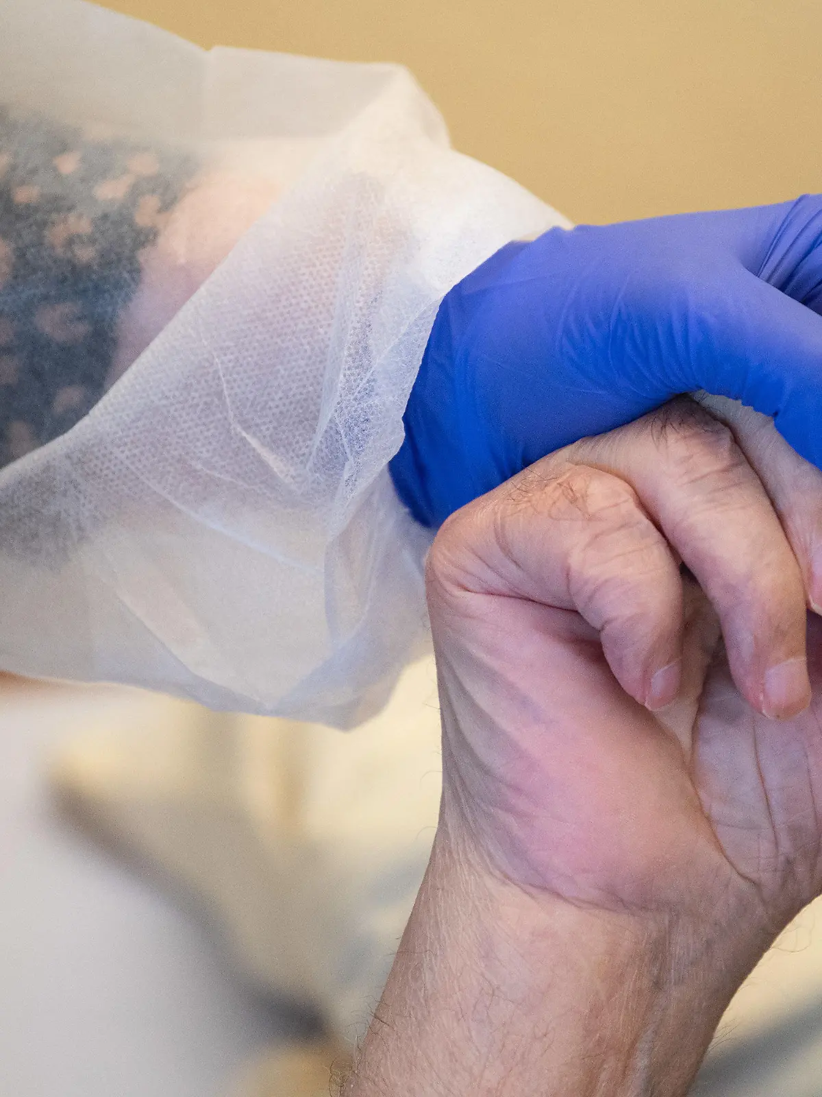ARCHIV - 18.11.2020, Baden-Württemberg, Tübingen: Eine Altenpflegerin in Schutzkleidung hält die Hand eines Bewohners. Die Altenpflegerinnen und -pfleger in Deutschland können auf bundesweit einheitliche und in vielen Fällen höhere Bezahlung hoffen. (Zu dpa: ««Stunde der Wahrheit» für höheren Pflegelohn») Foto: Sebastian Gollnow/dpa +++ dpa-Bildfunk +++