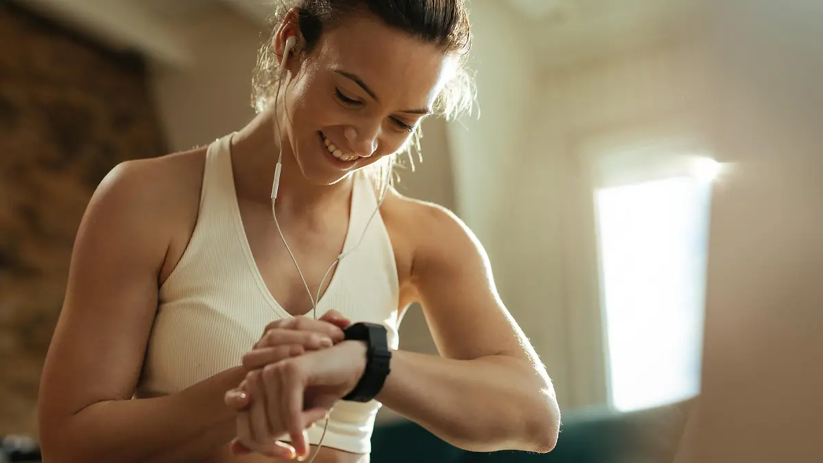 Happy athletic woman measuring heart rate on smart watch while resting after exercising at home.