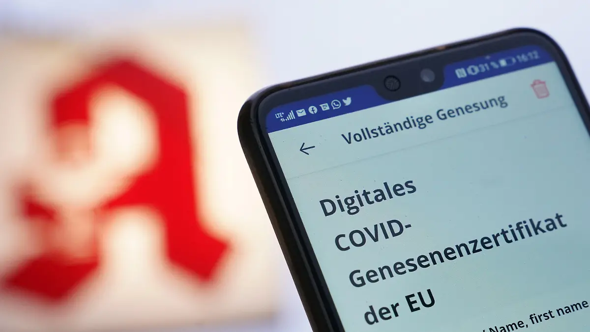 26.01.2022, ---: ILLUSTRATION - Ein Mann hält sein Smartphone mit einem digitalen Covid-Genesenenzertifikat vor einem Apotheken-Logo hoch. Die politische Entscheidung, dass Genesene nur noch knapp drei Monate als geschützt gelten, sorgt vielfach für Unmut und Unverständnis. (zu dpa: "Genesene, die unbekannten Wesen") Foto: Marcus Brandt/dpa +++ dpa-Bildfunk +++