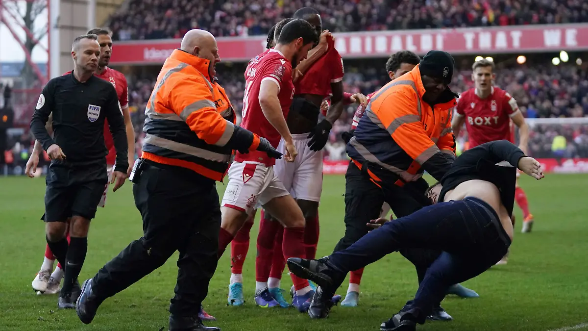 Stewards block a man who invaded the pitch as Nottingham Forest celebrate scoring their side's third goal, during the English FA Cup fourth round soccer match between Nottingham Forest and Leicester City at the City Ground, Nottingham, England, Sunday, Feb. 6, 2022. Police have arrested a man who appeared to attack Nottingham Forest players as they celebrated one of their goals in an FA Cup victory over Leicester. A supporter emerged from the away section of the City Ground before striking out at Forest players as they celebrated the third in a 4-1 win over the cup holders. (Tim Goode/PA via AP)