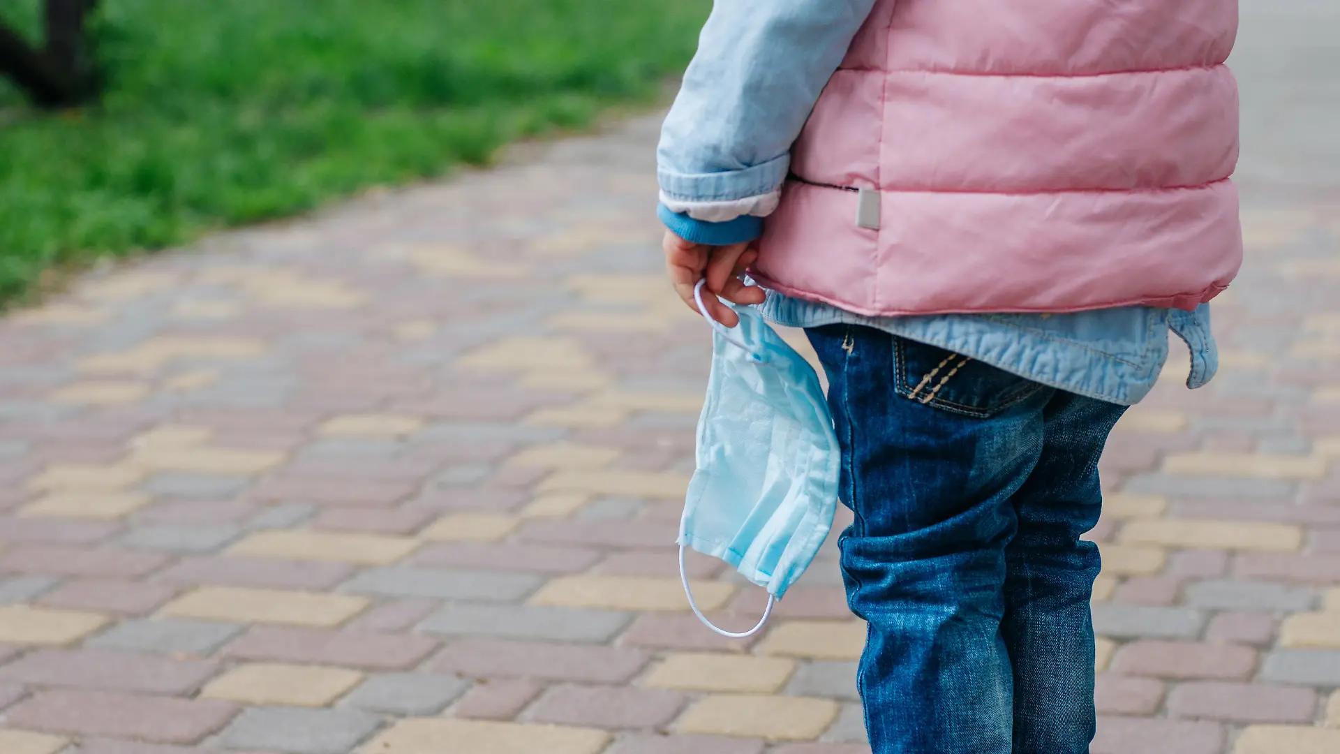 Close up of little girl holding protective face mask outside after the end of quarantine. Pandemic COVID-19 is over concept.