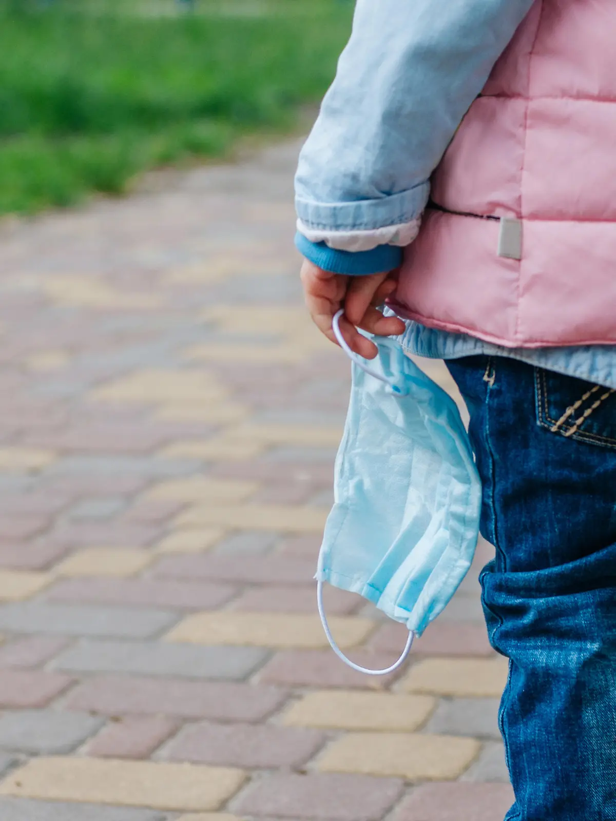 Close up of little girl holding protective face mask outside after the end of quarantine. Pandemic COVID-19 is over concept.