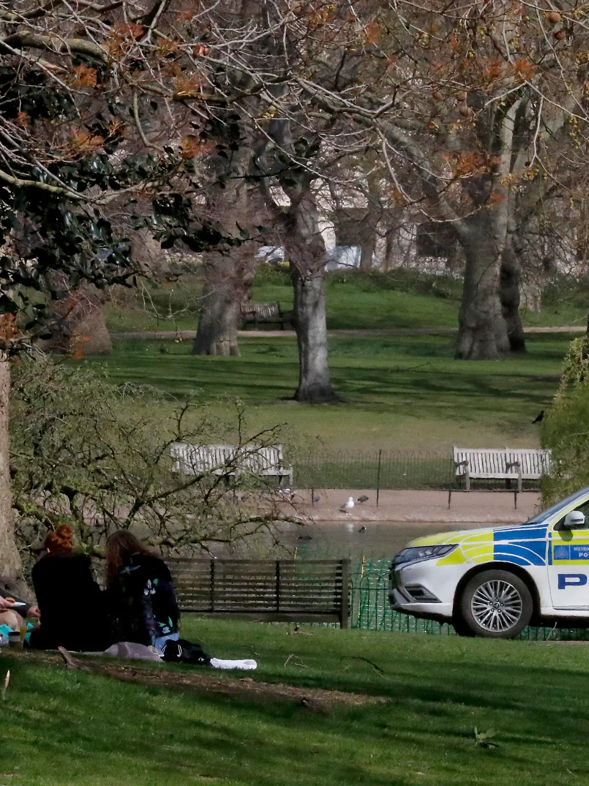 People observe coronavirus guidelines as a police car patrols nearby in central London, Monday, April 5, 2021.  The British government says all asymptomatic people in England will be able to get two free coronavirus tests per week, starting Friday, as a way to stamp out new outbreaks, and Prime Minister Boris Johnson said that regular testing would help "stop outbreaks in their tracks."(AP Photo/Frank Augstein)