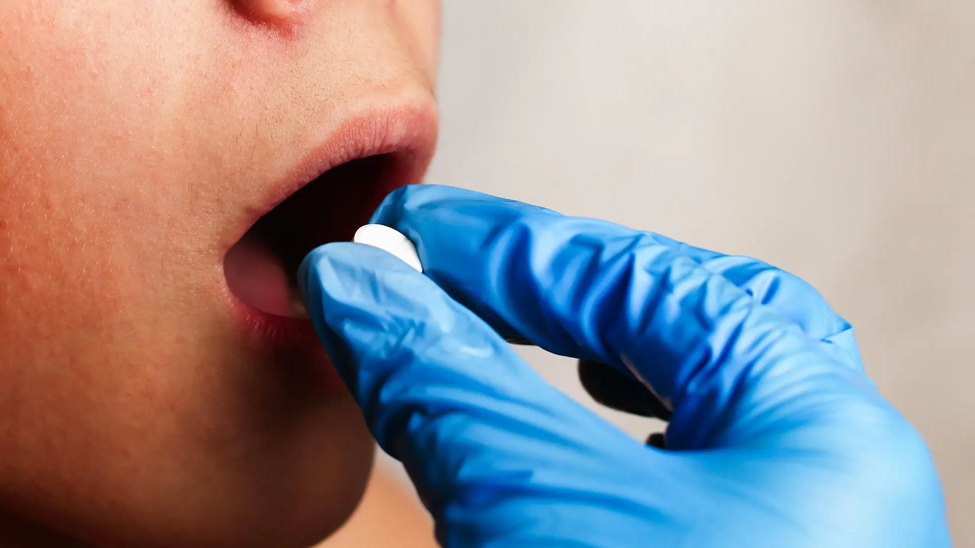 The doctor's hand puts a white pill in the patient's mouth close-up. High quality photo