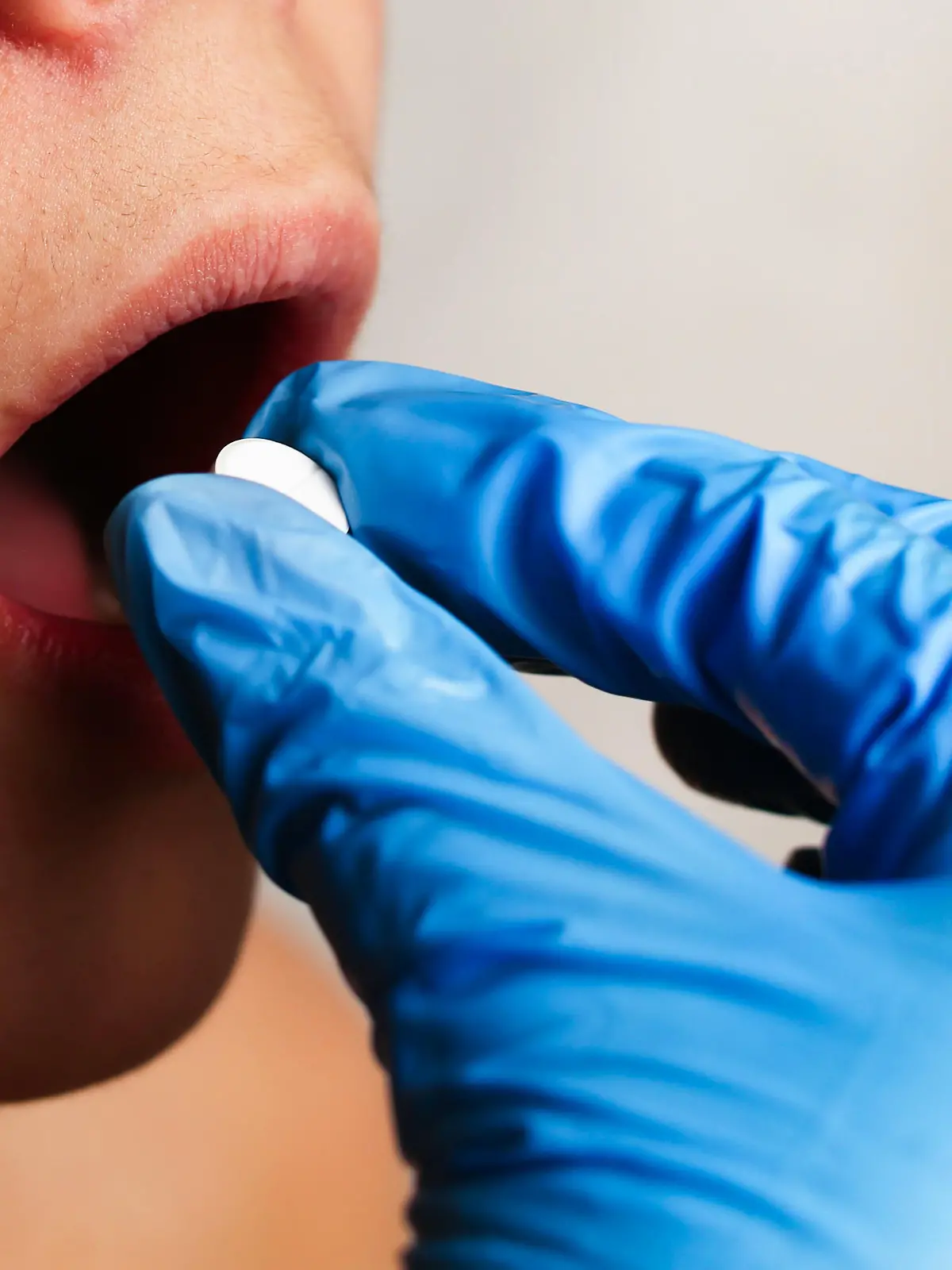 The doctor's hand puts a white pill in the patient's mouth close-up. High quality photo