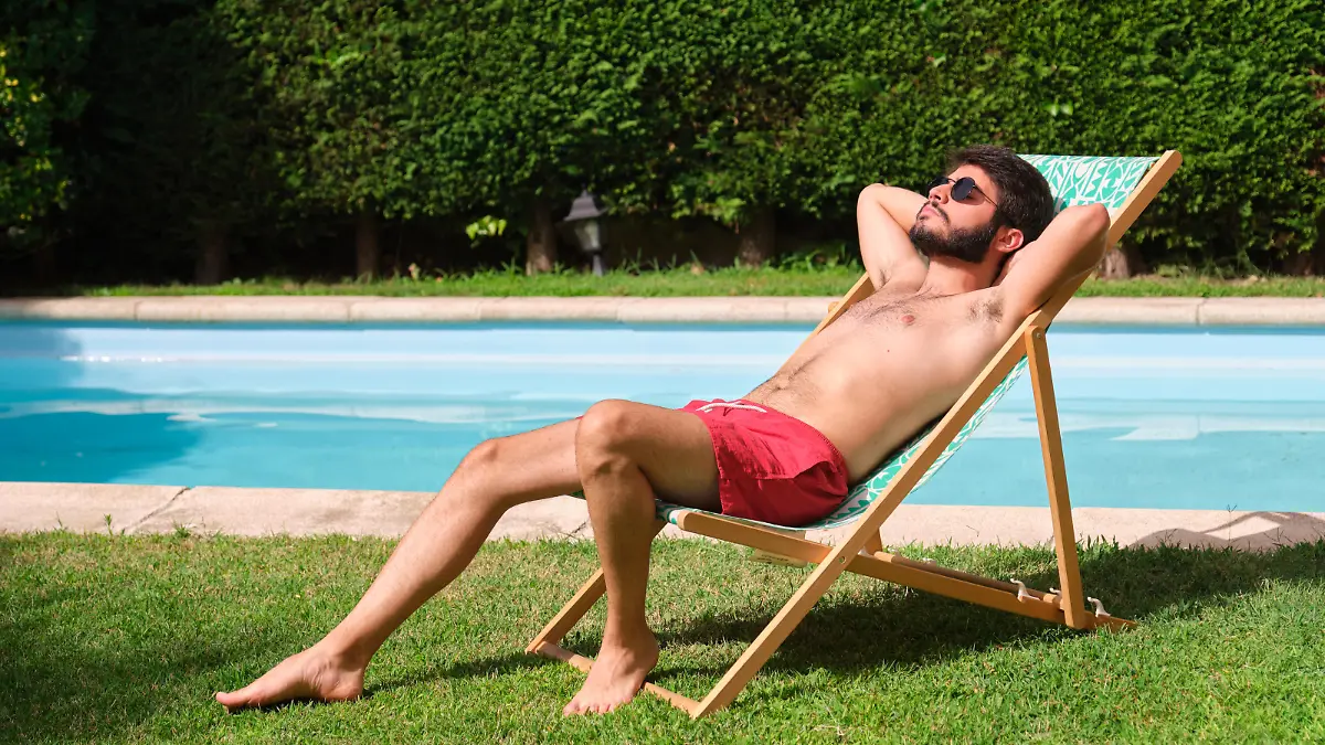 Young caucasian man with sunglasses sunbathing on a lounger by the swimming pool. Summertime.