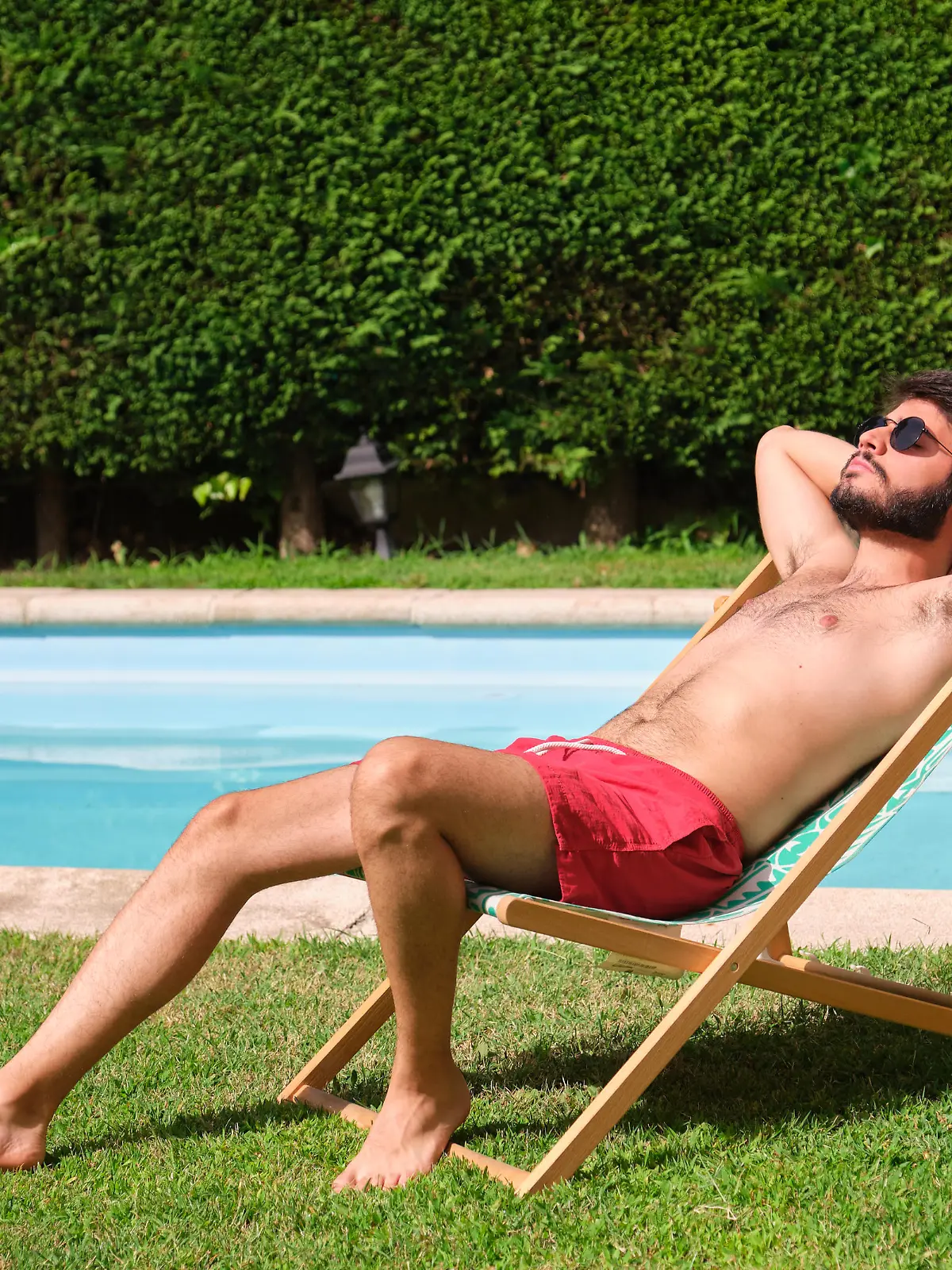 Young caucasian man with sunglasses sunbathing on a lounger by the swimming pool. Summertime.