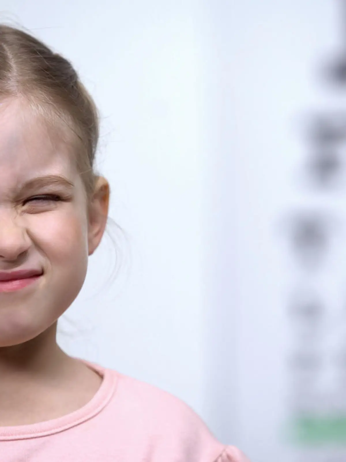 Small girl frowning, trying to see letter on vision testing table blurred vision