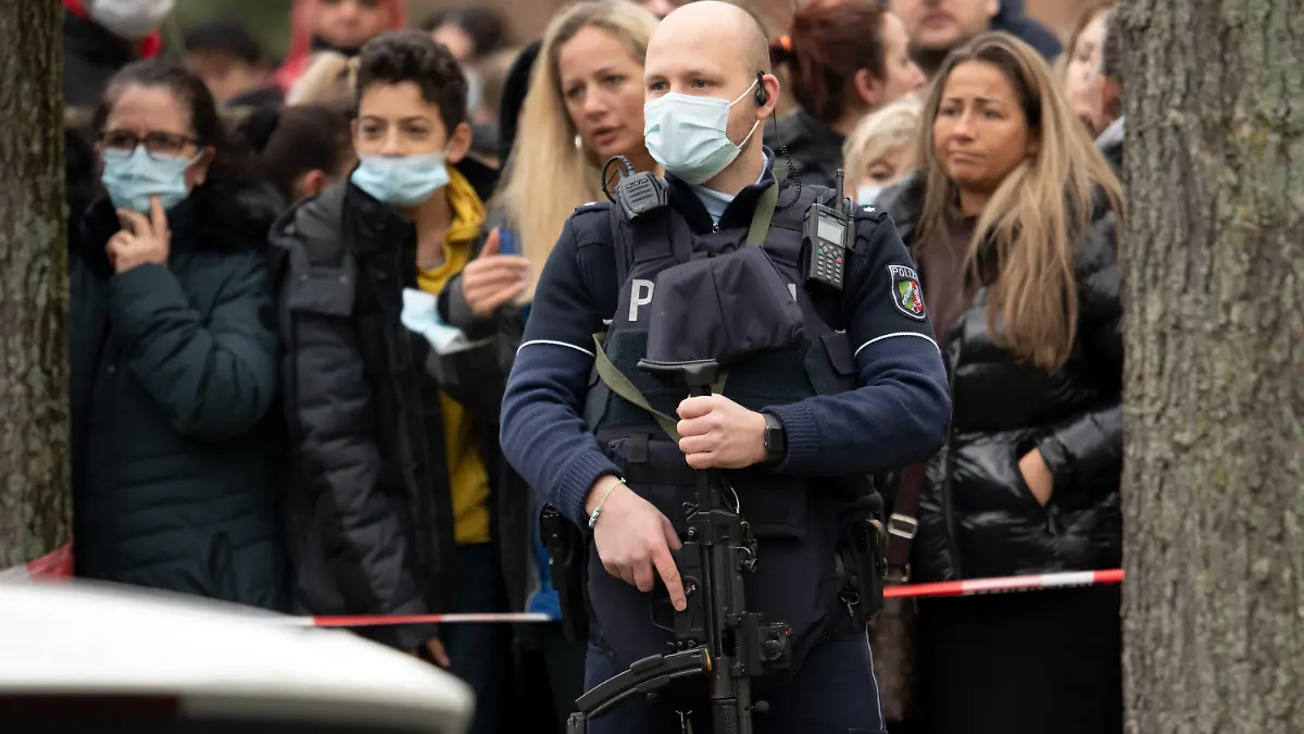 04.02.2022, Nordrhein-Westfalen, Köln: Ein Polizist mit einer Maschinenpistole sichert den Bereich, in dem Eltern und Schüler in der Nähe der Schule auf ihre Kinder warten. Die Schüler werden in Gruppen von Polizeikräften aus der Schule geführt. Nach einem Hinweis auf einen möglicherweise bewaffneten Mann läuft ein größerer Polizeieinsatz an einer Kölner Gesamtschule. Es sei Amok-Alarm ausgelöst worden. Foto: Federico Gambarini/dpa +++ dpa-Bildfunk +++