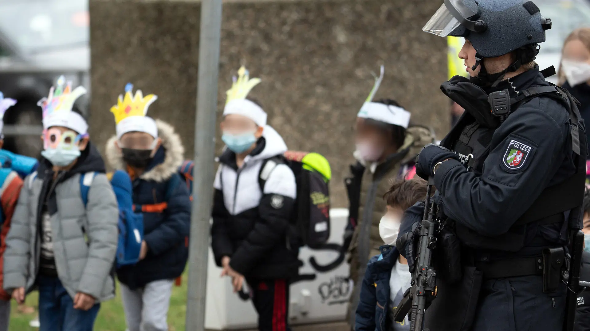 04.02.2022, Nordrhein-Westfalen, Köln: Ein Polizist mit einer Maschinenpistole sichert Schüler, die aus der Schule geführt werden. Nach einem Hinweis auf einen möglicherweise bewaffneten Mann läuft ein größerer Polizeieinsatz an einer Kölner Gesamtschule. Es sei Amok-Alarm ausgelöst worden. Foto: Federico Gambarini/dpa - ACHTUNG: Person(en) wurde(n) aus rechtlichen Gründen gepixelt +++ dpa-Bildfunk +++