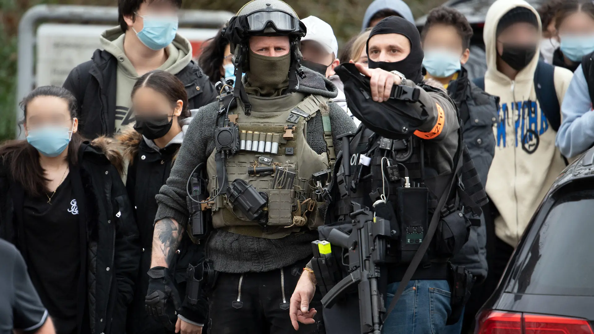 04.02.2022, Nordrhein-Westfalen, Köln: Polizisten mit Maschinenpistolen sichern Schüler, die aus der Schule geführt werden. Nach einem Hinweis auf einen möglicherweise bewaffneten Mann läuft ein größerer Polizeieinsatz an einer Kölner Gesamtschule. Es sei Amok-Alarm ausgelöst worden. Foto: Federico Gambarini/dpa - ACHTUNG: Person(en) wurde(n) aus rechtlichen Gründen gepixelt +++ dpa-Bildfunk +++