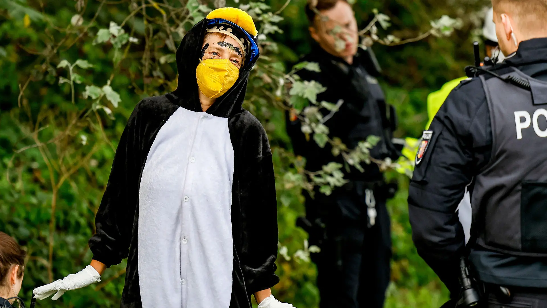 dpatopbilder - 25.08.2023, Schleswig-Holstein, Tinnum/Sylt: RECROP - Eine als Pinguin verkleidete Aktivistin der Gruppe ·Am Boden bleiben· tanzt vor Polizisten, nachdem die Gruppe versucht hat den Flughafen auf Sylt zu blockieren. Foto: Axel Heimken/dpa +++ dpa-Bildfunk +++