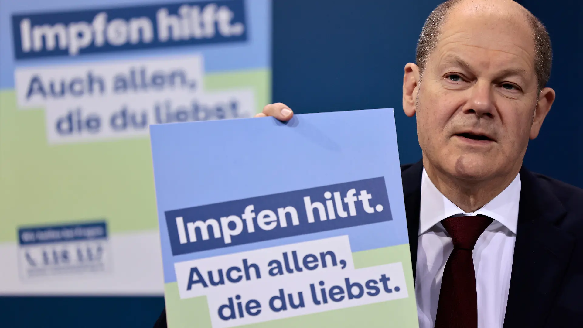24.01.2022, Berlin: Bundeskanzler Olaf Scholz (SPD) präsentiert ein Plakat für eine neue Impfkampagne während einer Pressekonferenz nach einem Treffen im Kanzleramt. Bundeskanzler Olaf Scholz traf sich mit den Ministerpräsidenten der 16 Bundesländer, um über die Coronavirus-Situation und die Maßnahmen zur Bekämpfung des Virus zu sprechen. Auf dem Plakat steht: "Impfen hilft. Sie hilft auch allen, die man liebt." Foto: Hannibal Hanschke/POOL AP/dpa +++ dpa-Bildfunk +++