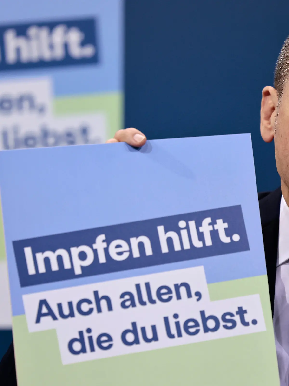 24.01.2022, Berlin: Bundeskanzler Olaf Scholz (SPD) präsentiert ein Plakat für eine neue Impfkampagne während einer Pressekonferenz nach einem Treffen im Kanzleramt. Bundeskanzler Olaf Scholz traf sich mit den Ministerpräsidenten der 16 Bundesländer, um über die Coronavirus-Situation und die Maßnahmen zur Bekämpfung des Virus zu sprechen. Auf dem Plakat steht: "Impfen hilft. Sie hilft auch allen, die man liebt." Foto: Hannibal Hanschke/POOL AP/dpa +++ dpa-Bildfunk +++
